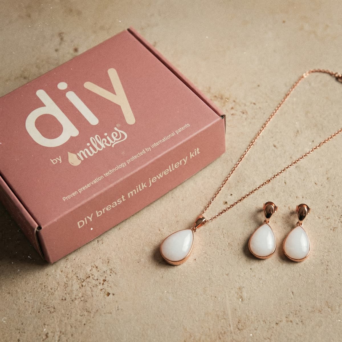 Kit DIY by MILKIES come regalo donna incinta: set per gioielli con latte materno con collana e orecchini a goccia in oro rosa accanto alla scatola rosa.