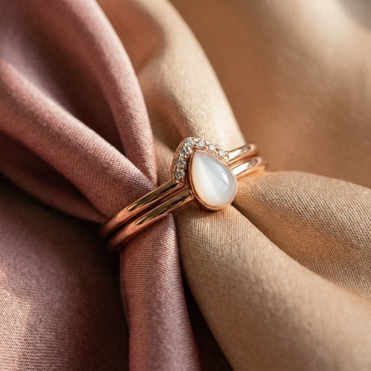 Anello in oro rosa con pietra a goccia color latte e piccoli cristalli su tessuto satinato rosa e beige, elegante ricordo maternità da indossare ogni giorno.