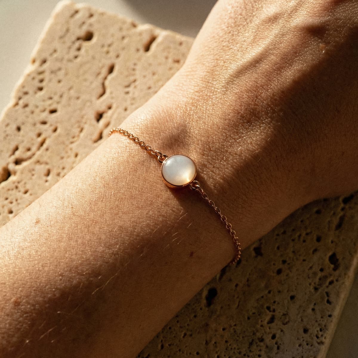 Dettaglio di un bracciale delicato in oro rosa con pietra rotonda lattiginosa indossato al polso, esempio di braccialetti latte materno fai da te illuminati da luce naturale.