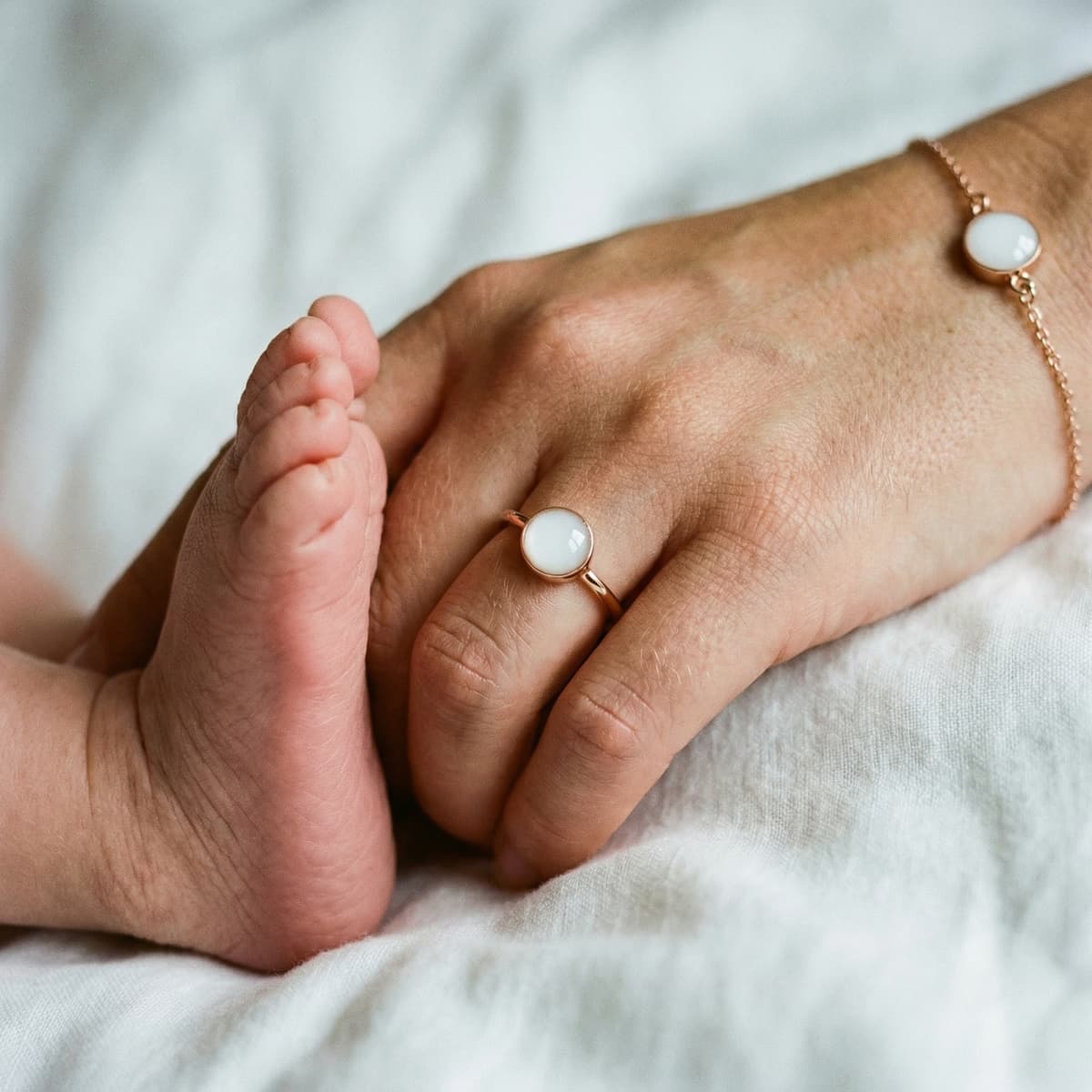 Mano di mamma con anello e bracciale in oro rosa che tiene il piedino del neonato, idea delicata per creare gioielli latte materno come ricordo personale.
