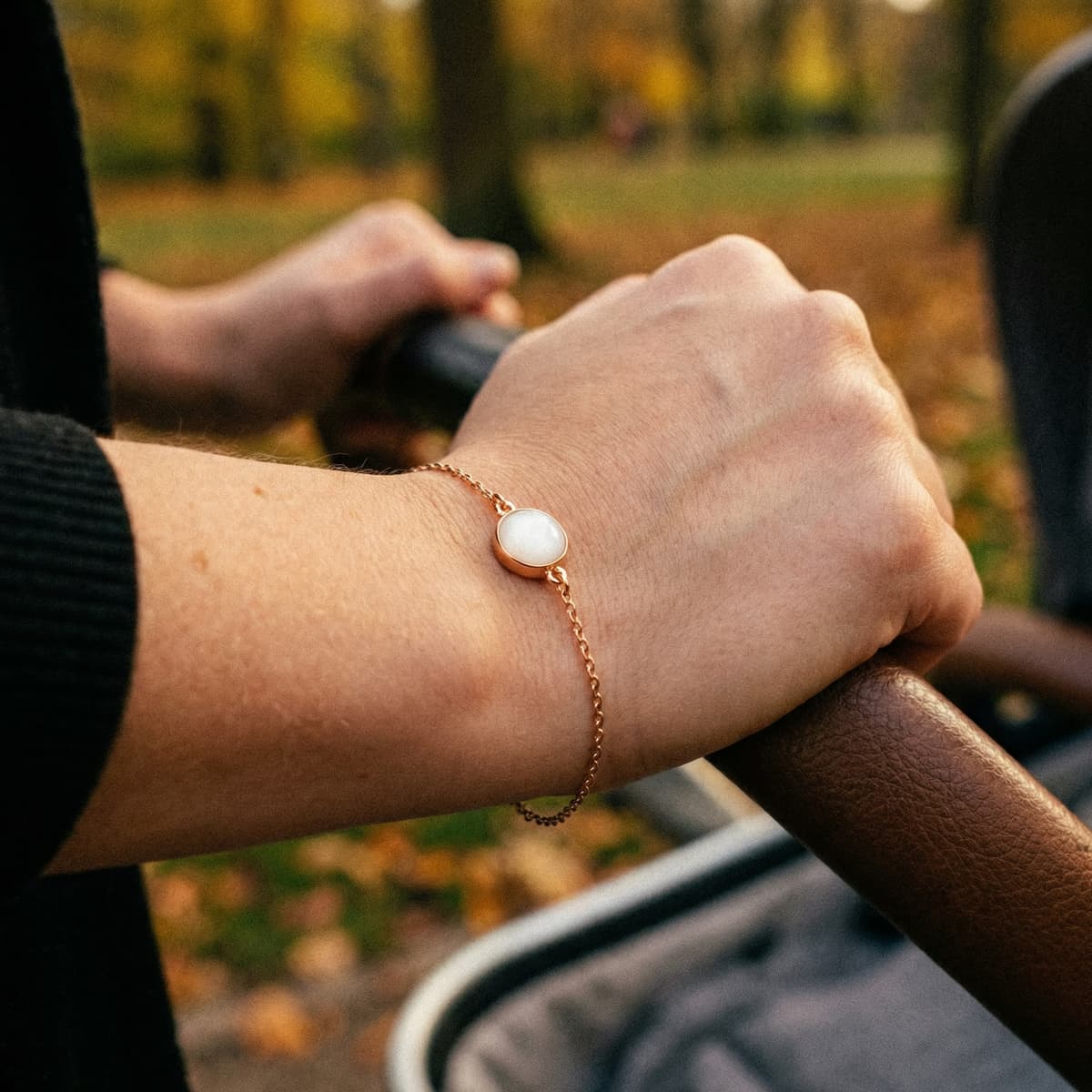 Donna all’aperto che spinge un passeggino e indossa un delicato bracciale dorato con cabochon bianco realizzato con kit bracciale latte materno come gioiello ricordo.