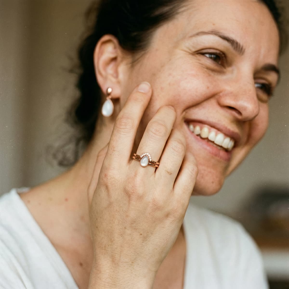 Donna sorridente indossa un anello con pietra color latte e orecchini coordinati, esempio di ricordo creato a casa con un kit fai da te anello latte materno per conservare un momento speciale in modo semplice e personale.