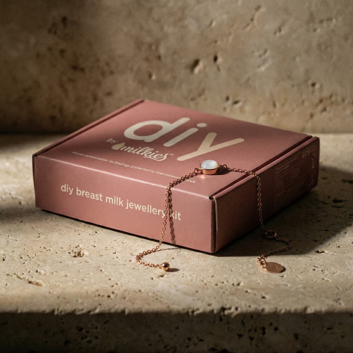 Scatola rosa DIY by MILKIES con collana in catena dorata appoggiata sopra, ideale come kit per creare bracciale latte materno e gioielli ricordo fai-da-te con latte materno.