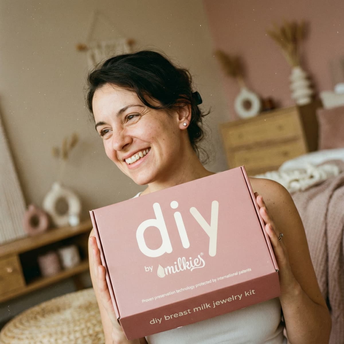 Donna sorridente con in mano il kit DIY by MILKIES, soluzione pratica e discreta per creare a casa orecchini di latte materno fai da te e altri gioielli ricordo con tecnologia di conservazione brevettata.