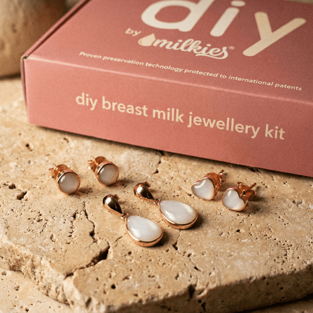 Kit DIY by Milkies per creare gioielli con latte materno, con orecchini latte materno fai da te e pendenti a goccia in montatura color oro rosa, mostrato davanti alla confezione “DIY Breast Milk Jewellery Kit”.