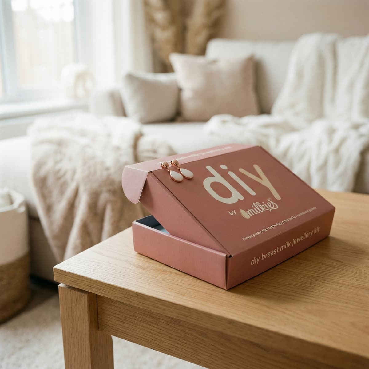 Scatola rosa con kit DIY by MILKIES e orecchini su un tavolino in un salotto luminoso, ideale come regalo fine allattamento per creare a casa un gioiello ricordo.