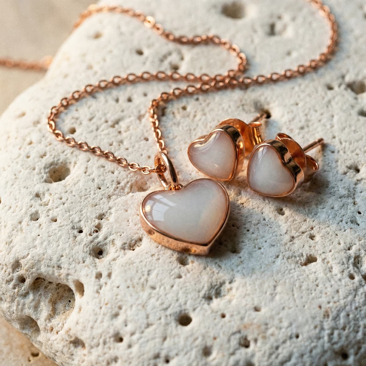 Collana e orecchini a cuore in tonalità oro rosa con pietra lattiginosa su sfondo in pietra, idea regalo originale nascita elegante e simbolica per neo mamma
